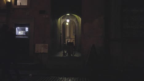 People-Walk-at-Old-Town-Warsaw-Poland,-Wheelchair-on-a-Narrow-Dark-Night-Street