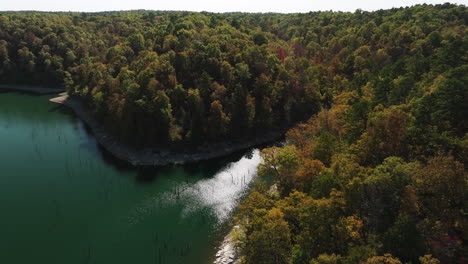 Beaver-lake-Eagle-Hollow-cave-aerial-view-over-dense-forest,-sunny-day