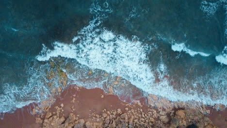 Aerial-top-down-shot-of-ocean-waves-crushing-on-rocks-on-shore