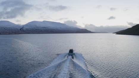 Färöer-Inseln,-4k-Luftverfolgung-Hinter-Einem-Fischerboot-Mit-Schneebedeckten-Bergen-Im-Hintergrund