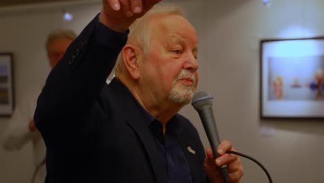 Older-white-elderly-man-holding-microphone-talking-speaking-handheld-closeup