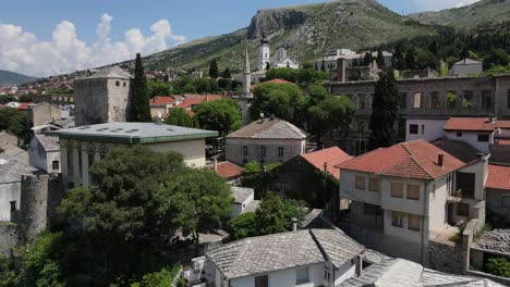 Drone-view-of-the-Mostar-bridge-between-historical-Ottoman-buildings,-tourists-visiting-the-historical-bridge