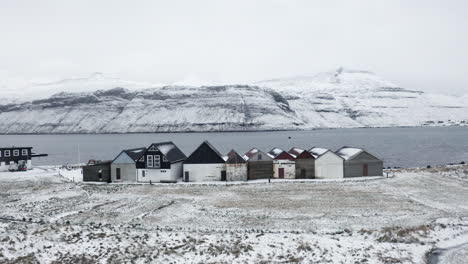 Faroe-Islands,-4K-Aerial-of-Hósvík-Boathouses-as-we-slowly-pull-back-to-reveal-more-of-the-surrooundong-landscape