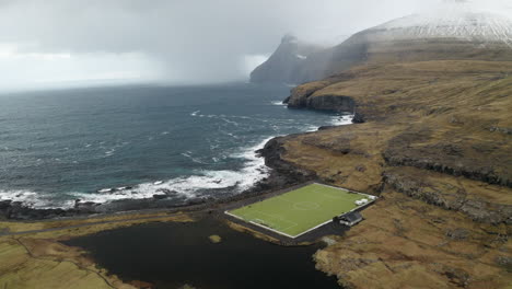 Faroe-Islands,-4K-Aerial-of-Niðara-Vatn-football-pitch-with-beautiful-mountains-in-the-background