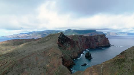 Acantilado-De-La-Isla-Con-Un-Pequeño-Faro-Distante-Con-Niebla-Y-Nubes-Al-Fondo