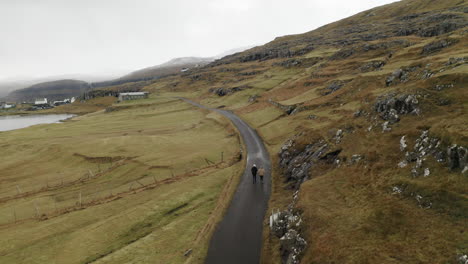 Faroe-Islands,-4K-Aerial-of-Niðara-Vatn-with-two-people-walking-along-a-road