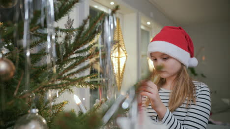 Young-blonde-girl-in-santa-hat-decorates-christmas-tree,-close-up