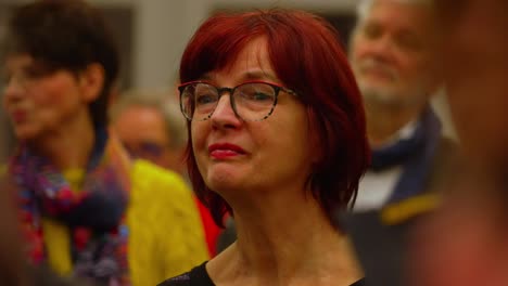 Red-haired-older-lady-with-glasses-in-crowd-close-up-carefully-listening
