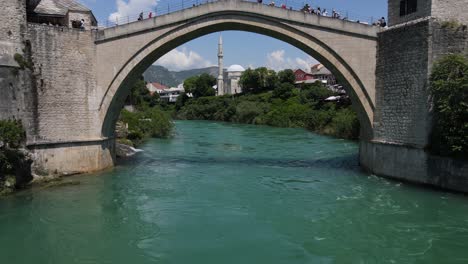Aerial-view-of-the-historical-Mostar-bridge-built-over-the-river-in-the-city-of-Bosnia,-people-on-the-tourist-bridge