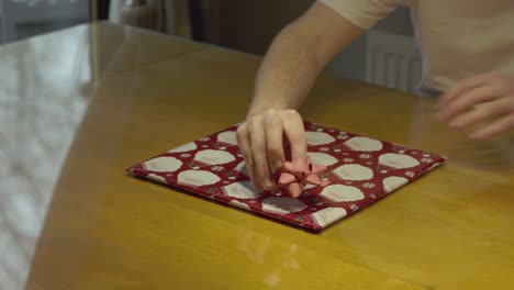 Static-shot-of-hands-applying-a-bow-onto-a-wrapped-vinyl-Christmas-gift
