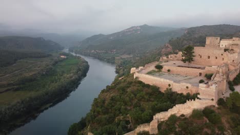 Die-Drohnenaufnahme-Der-Burg-Miravet-Zeigt-Den-Fluss-Ebro-Dahinter