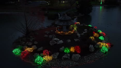 Green,-red,-yellow-Christmas-lights-in-garden-with-pond-during-December-night-in-USA