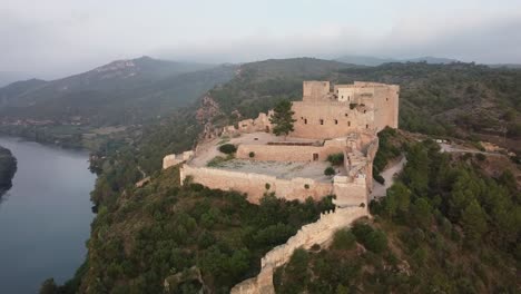Drohnenansicht-Der-Burg-Miravet-Und-Des-Flusses-Ebro-An-Einem-Nebligen-Tag