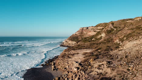 Scenic-drone-footage-unveils-a-coastal-hill,-waves-caressing-its-side