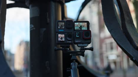 Comparison-of-four-small-compact-action-cameras-mounted-together-on-tripod-with-cityscape-in-background