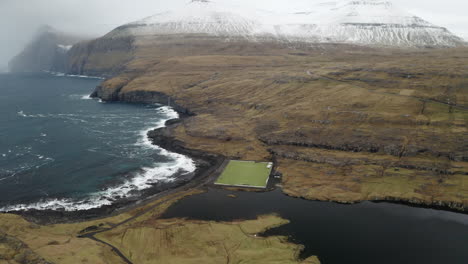 Faroe-Islands,-4K-Aerial-Orbit-of-Niðara-Vatn-football-pitch-with-beautiful-mountains-in-the-background