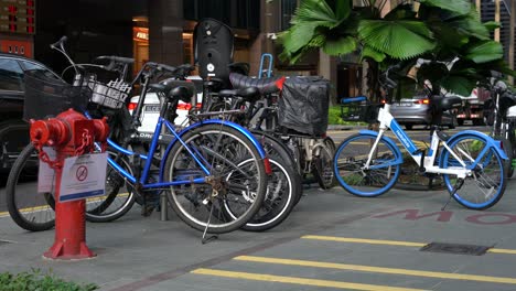 Bicicletas-Estacionadas-Cerca-De-La-Boca-De-Incendios-Roja-Y-Con-El-Telón-De-Fondo-De-Autos-En-Movimiento-En-Raffles-Place,-Singapur