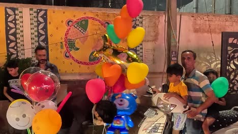 Filmischer-Ruß:-Ein-Händler-Verkauft-Nachts-Bunte-Luftballons-Auf-Einer-Süßen-Straße,-Auf-Der-Kleine-Kinder-Einkaufen