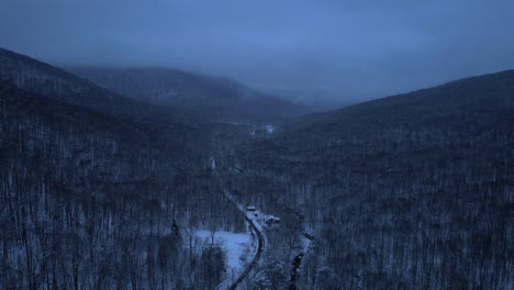 Beautiful-aerial-drone-video-footage-of-a-mountain-road-through-the-Appalachian-Mountains-covered-in-snow-at-night-during-evening
