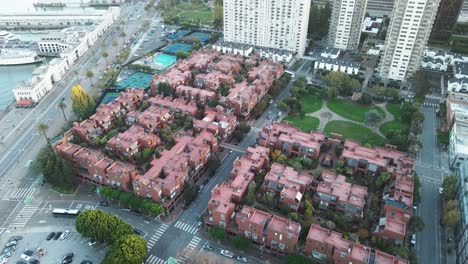 Aerial-view-of-a-residential-area-with-rows-of-townhouses,-surrounded-by-high-rise-buildings-and-streets,-showcasing-urban-living