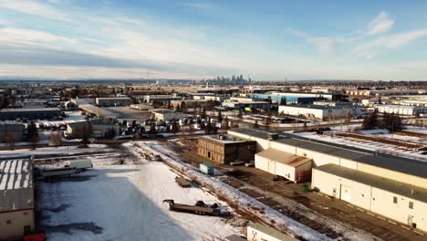 Flying-Over-Winter-Warehouses-with-a-View-of-Downtown-Calgary,-Alberta,-Canada