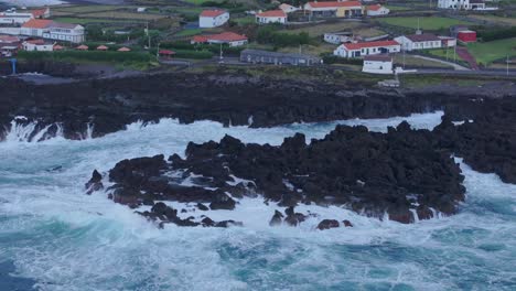 Reveal-shot-of-Fajã-Grande-town-at-Flores-island-with-rough-sea,-aerial