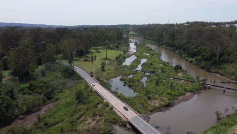 Drone-flying-over-a-highway-bridge-over-a-brown-river-a-pipeline-is-also-visible