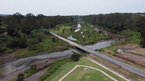 Aerial-view-of-a-brown-river-with-a-bridge-and-a-pipeline-crossing-over-it