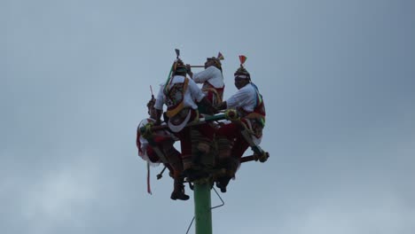 close-up-Papantla-dancers-on-the-top-of-the-pole,-playing-drums-during-a-cloudy-day