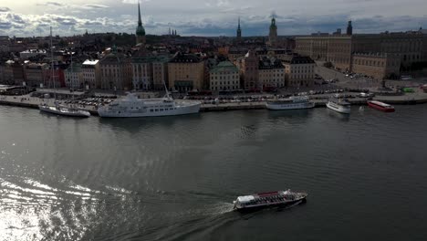 Drohnenaufnahmen-Eines-Bootes-Auf-Den-Gewässern-Von-Stockholm,-Mit-Der-Altstadt-Von-Gamla-Stan-Im-Hintergrund