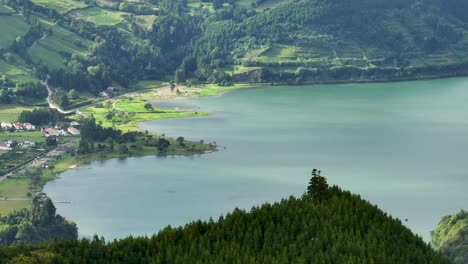 Aerial-telephoto-view-of-village-on-volcanic-crater-lake-shore,-Sete-Cidades