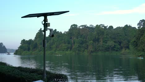 Surveillance-cameras-powered-by-solar-panels,-the-movement-of-gentle-waves,-and-the-background-of-the-beautiful-view-of-Macritchie-Reservoir-in-Singapore
