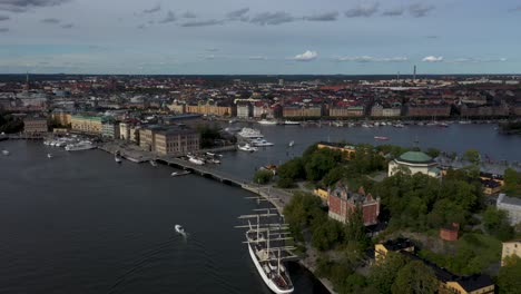 Drone-footage-of-the-Skeppsholmsbron,-an-iron-bridge-featuring-a-gilded-crown-along-a-side-railing-with-views-of-the-Gamla-Stan-old-town-in-the-background