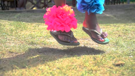 Feet-in-Sandals-Jumping-Dancing-on-the-Grass-with-Festive-Colorfull-Decorations-on-the-Legs,-Slow-Motion