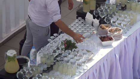 Bartenders-preparing-Summer-Party-Service-on-a-Prepared-Counter-full-of-Glasses,-Slow-Motion