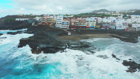 Luftaufnahme-Im-Orbit-über-Dem-Strand-Und-Den-Häusern-An-Der-Küste-Von-El-Puertillo-Im-Norden-Der-Insel-Gran-Canaria-Und-Mit-Großen-Wellen,-Die-Die-Küste-Treffen