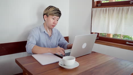 Eine-Erwachsene-Frau-Mit-Kurzen-Haaren-Sitzt-Tagsüber-Im-Café-Und-Nimmt-Sich-Notizen-Zum-Online-Treffen-Mit-Laptop