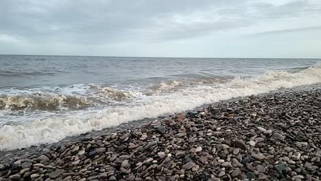 Sandy-ocean-waves-crashing-slow-motion-on-Welsh-pebble-beach-in-windy-autumn-season