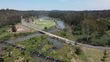 Drohne-Fliegt-über-Eine-Autobahn,-Eine-Pipeline-Und-Eine-Brücke-über-Einen-Kürzlich-überfluteten-Fluss-Auf-Einen-Grünen-Park-Zu