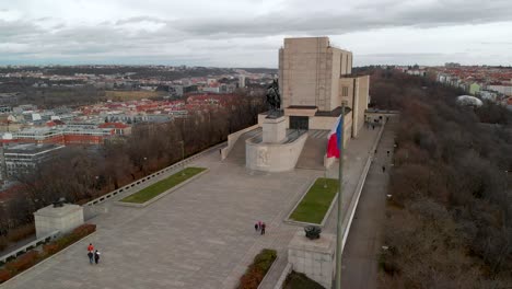 Prague,-Vitkov-Hill,-Aerial-View-of-Czech-National-Monument-and-Waving-Country-Flag-on-Cloudy-Autumn-Evening