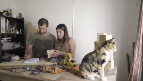 Young-couple-plans-out-a-home-improvement-carpentry-project-together-with-pet-cat-in-the-foreground