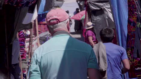 Old-man-gringo-walking-through-Chichi-market-in-Guatemala,-uring-daytime
