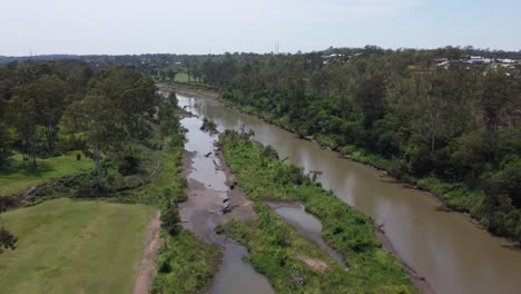 Aerial-view-of-a-small-brown-river-with-private-homes-in-the-background