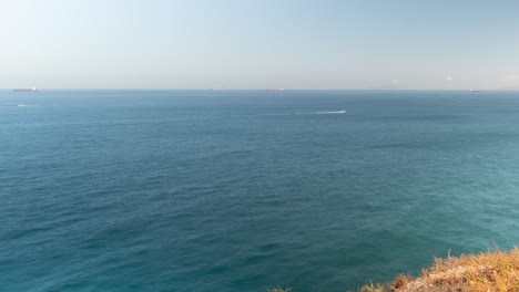 Blue-ocean-with-boats-and-lighthouse-on-rocky-cliffs,-pan-time-lapse-view
