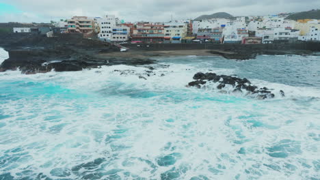 Luftaufnahme-Im-Orbit-über-Dem-Strand-Und-Den-Häusern-An-Der-Küste-Von-El-Puertillo-Im-Norden-Der-Insel-Gran-Canaria-Und-Mit-Den-Wellen,-Die-Auf-Die-Felsen-Schlagen