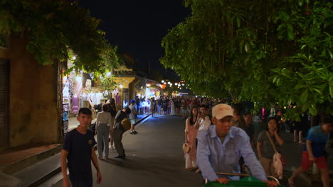 POV-shot-of-local-people-and-tourists-walking-tour-in-the-ancient-town-of-Hoi-An-decorated-with-colorful-lanterns-alongside-river-at-night,-Vietnam