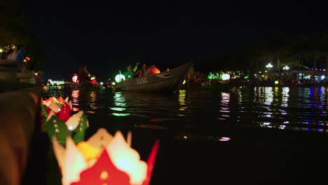 Handmade-Paper-lanterns-floating-in-Hoin-river-shore-with-tourists-taking-ride-on-sampan-boats-during-light-festival,-Hoi-An,-Vietnam