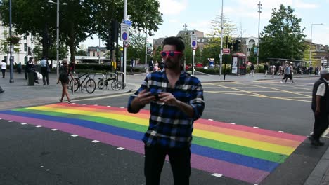 Handsome-man-taking-selfie-in-front-of-rainbow-pedestrian-crossing-in-London-for-pride-month,-eye-level-shot,-static-camera,-day,-real-time