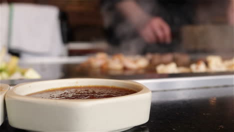 Close-up-of-dipping-sauce-dish-while-Japanese-chef-cooks-food-on-a-Teppanyaki-grill