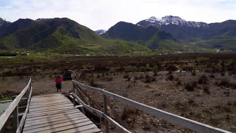 Mujer-De-La-Comunidad-Mapuche-Cruzando-Un-Puente-De-Madera-Con-Un-Hermoso-Paisaje-Montañoso-Al-Fondo.